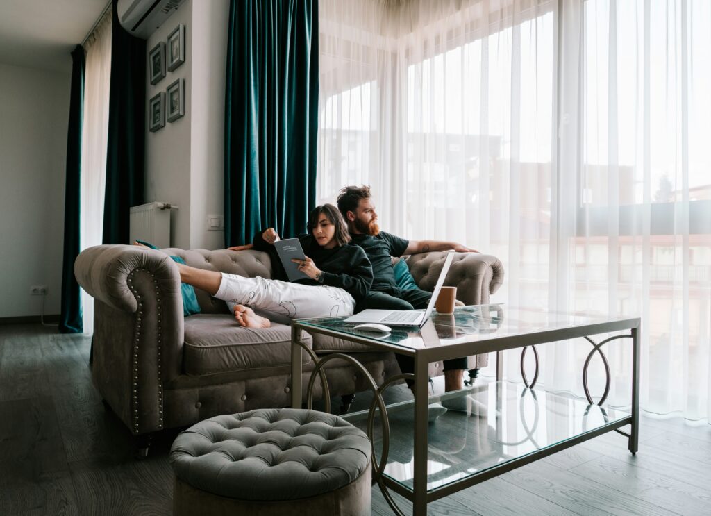 A tired couple at either end of a sofa — fertility stress rarely lands the same way on two people