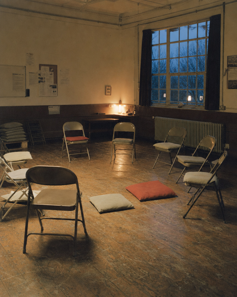 An empty meditation circle with one chair pushed back — the person who left, and the teacher who notices